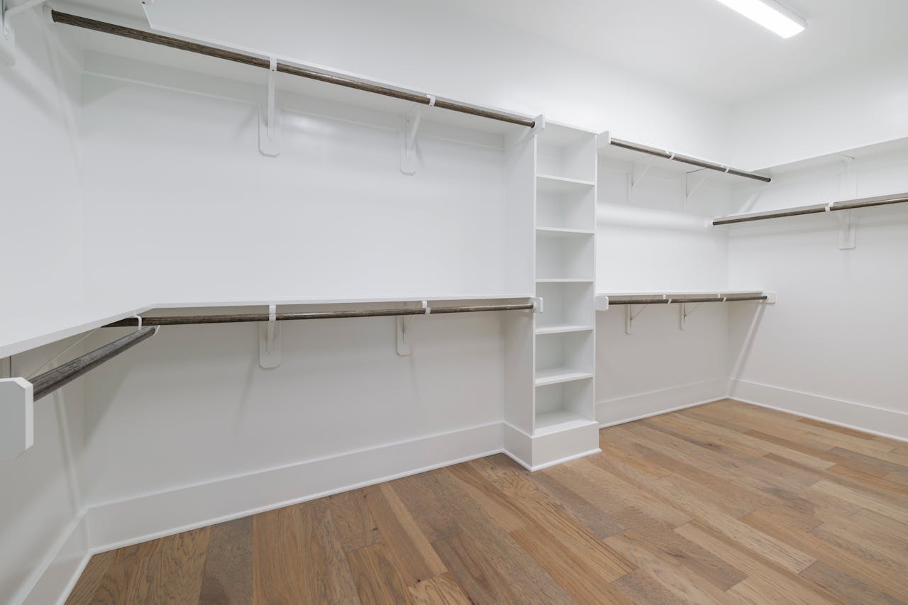 Modern empty walk-in closet with wooden flooring and white shelving.